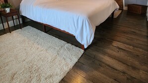 Un dormitorio con una cama grande, piso de madera, una alfombra blanca y una pared de ladrillo.
