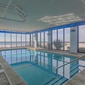 Piscina interior con vistas despejadas a la playa a través de amplios ventanales.