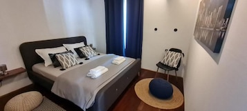 A neatly arranged bedroom with a bed, pillows, a chair, a hat, and a painting on the wall.