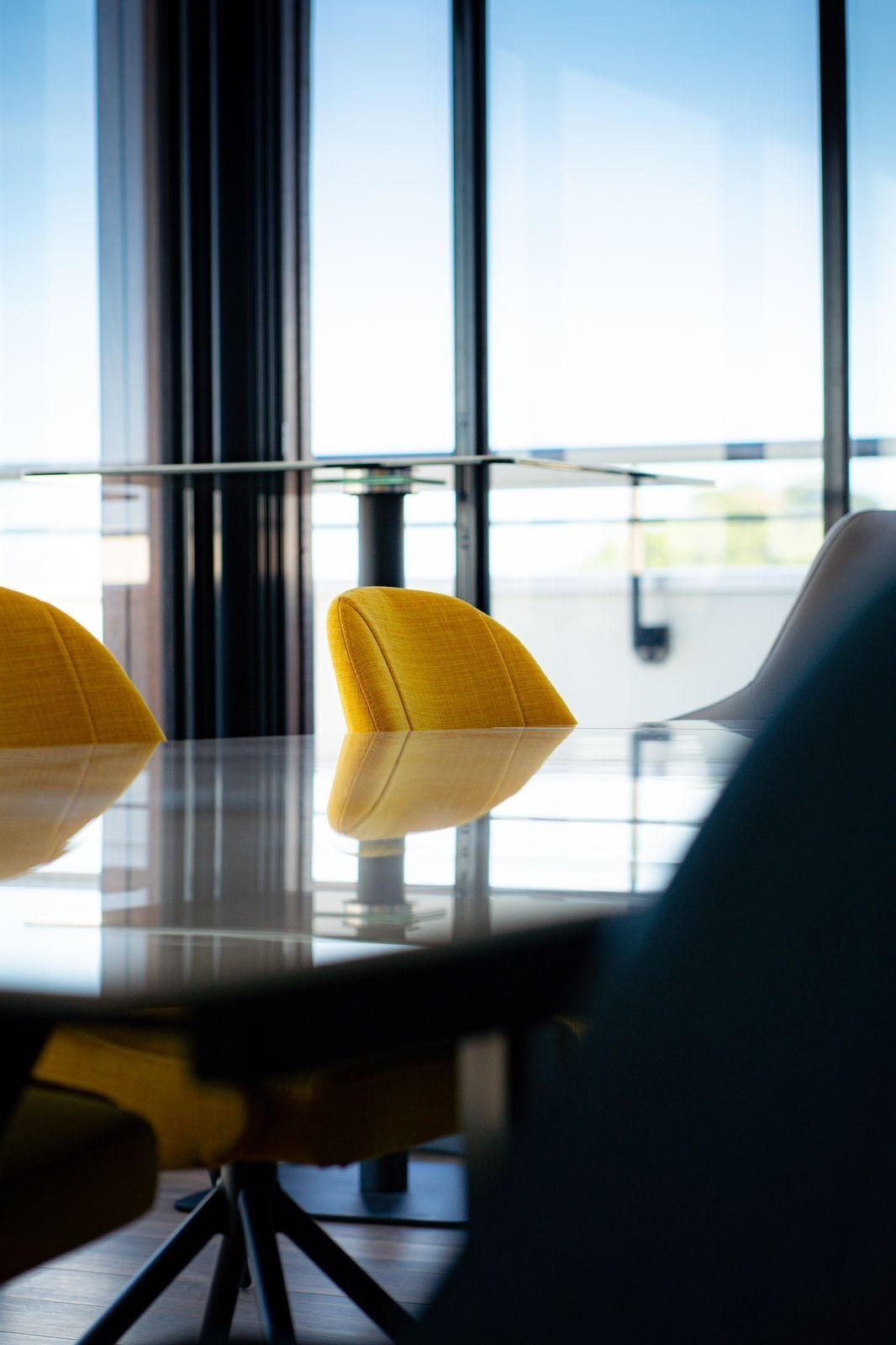 Een moderne vergaderruimte met een glazen tafel en twee gele stoelen.
