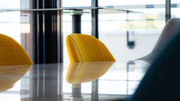 Een moderne vergaderruimte met een glazen tafel en twee gele stoelen.