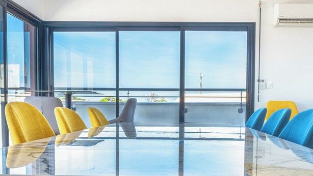 A conference room with a glass table, yellow and blue chairs, and large windows with a view of the city.