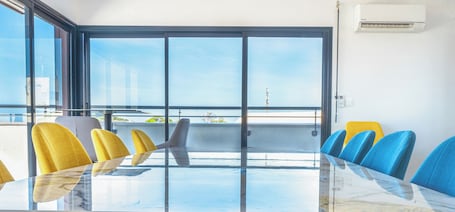 A conference room with a glass table, yellow and blue chairs, and large windows with a view of the city.