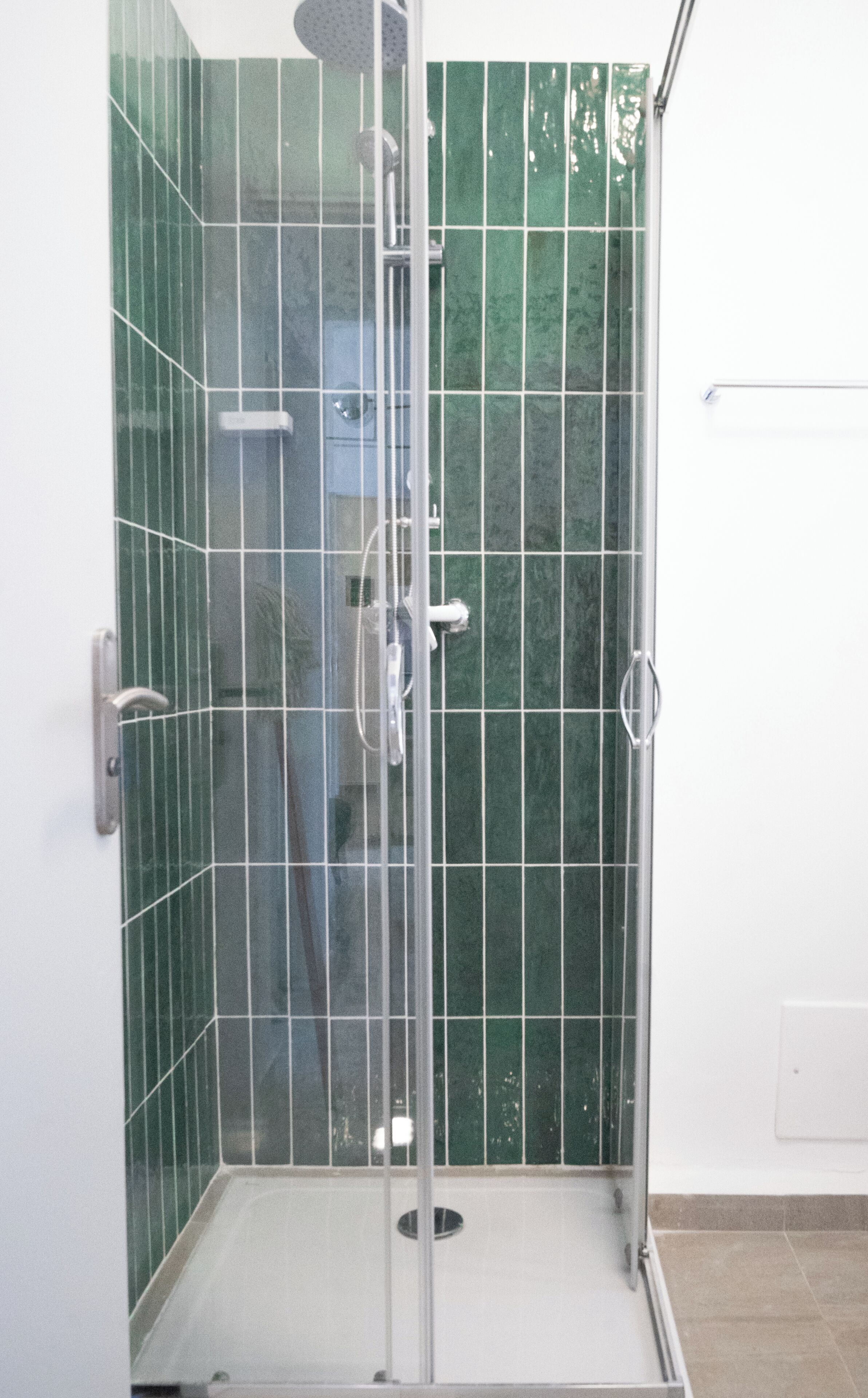 A glass-enclosed shower stall with a tiled wall and a metal door.