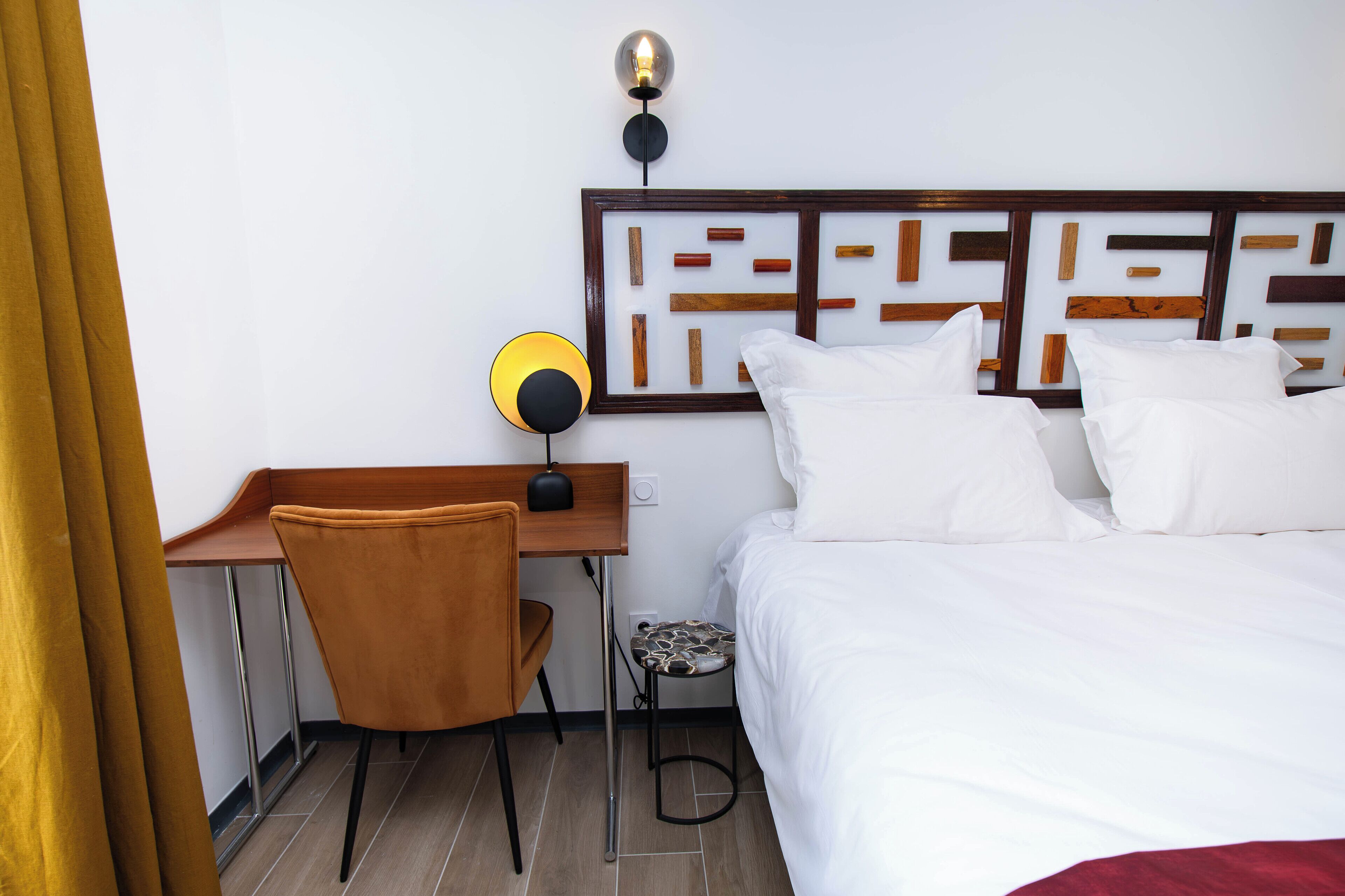 A hotel room with a bed, a desk, a chair, and a wall-mounted lamp.