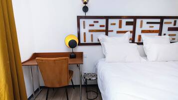 A hotel room with a bed, a desk, a chair, and a wall-mounted lamp.