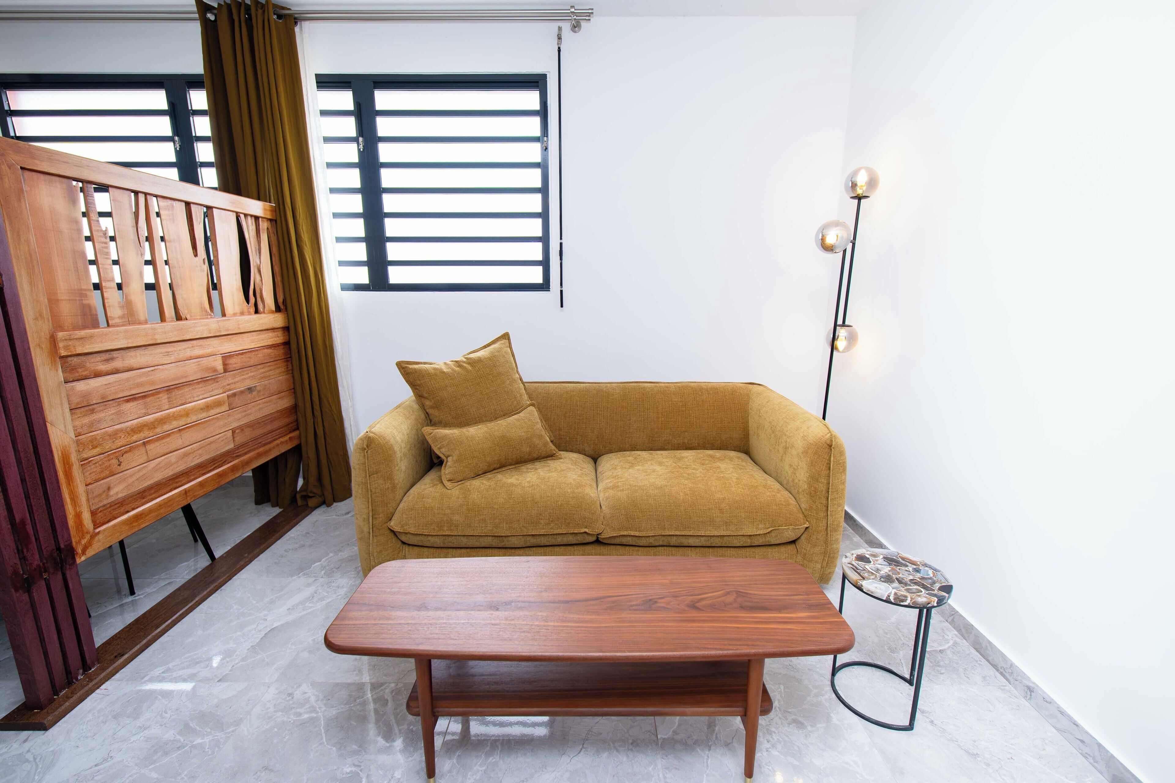 Una sala de estar con un sofá, una mesa de centro de madera, un taburete pequeño y una lámpara de pie.