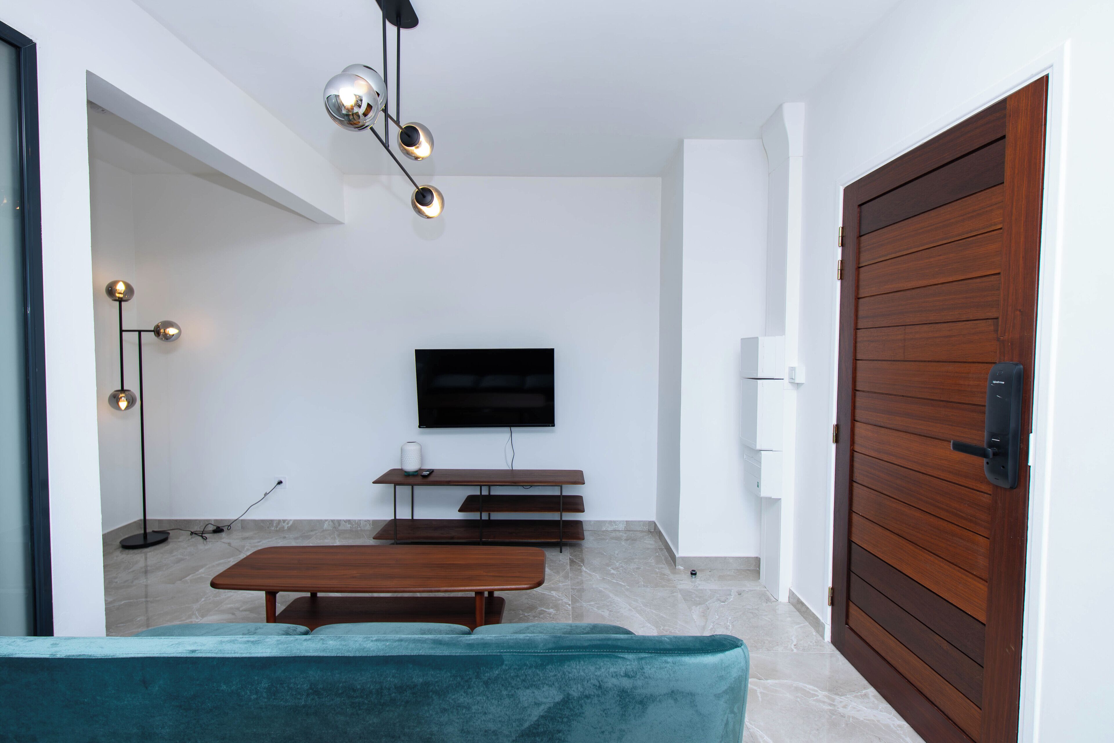 A modern living room with a flat-screen TV, wooden bench, and a teal sofa.