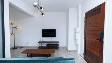 A modern living room with a flat-screen TV, wooden bench, and a teal sofa.