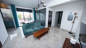 A modern living room with a green sofa, a wooden coffee table, and a TV stand with a remote control.