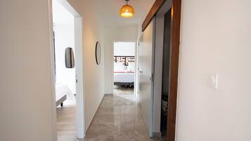 A hallway with a bed, a door, and a hanging light fixture.