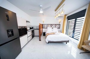 Una habitación de hotel moderna con cama, kitchenette, ventilador de techo y un gran ventanal con cortinas.