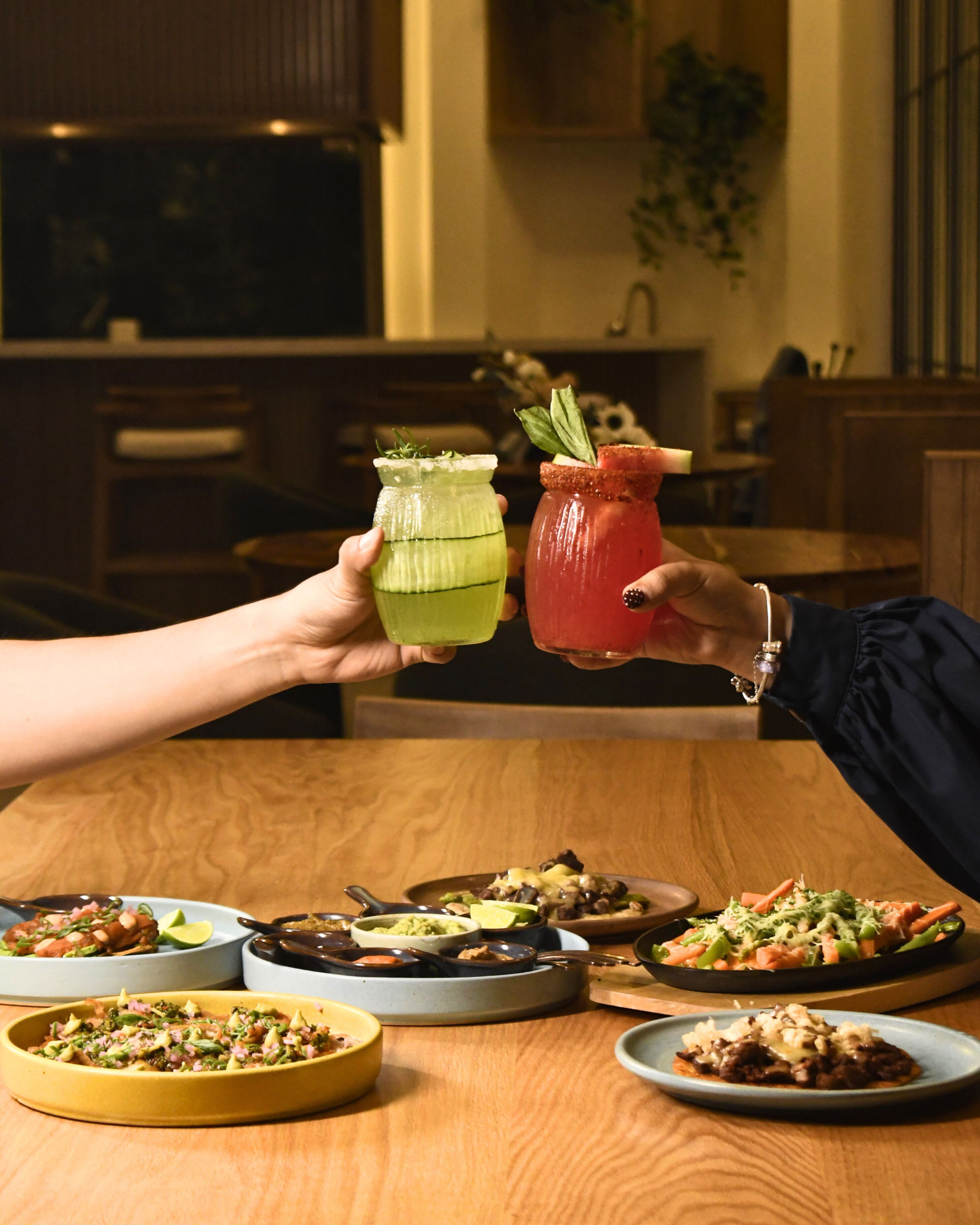 A dining table with various dishes and two hands holding cocktail glasses.