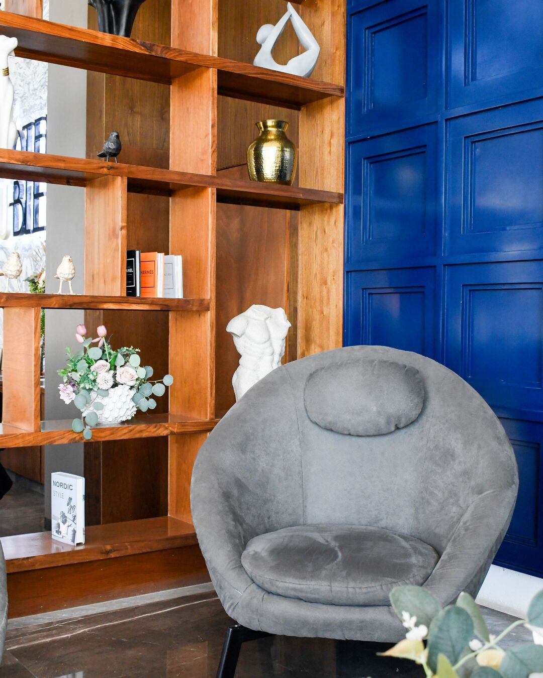 A room with a grey armchair, wooden shelves with decorative items, and a blue door.