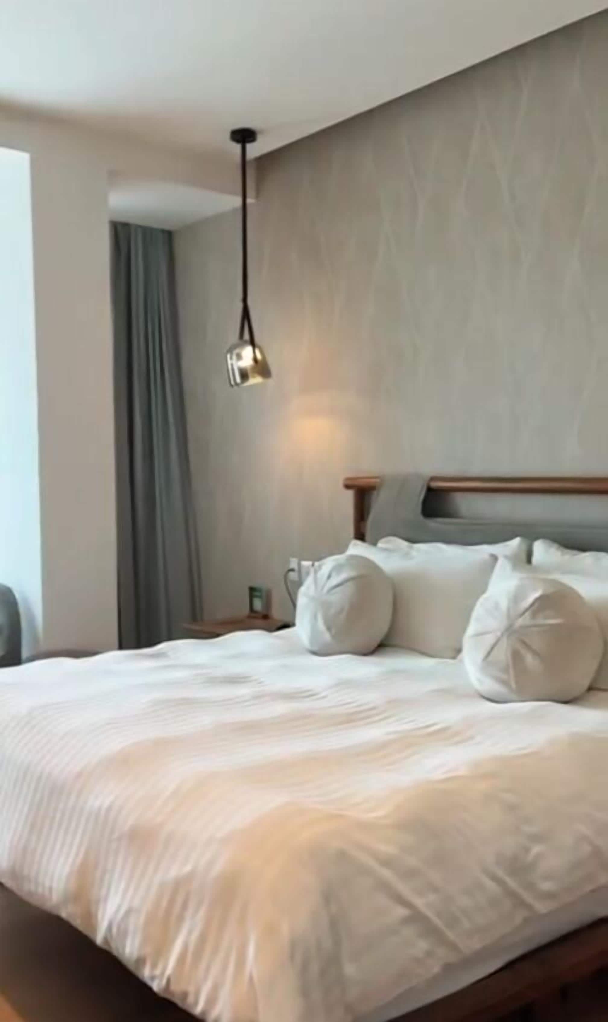 A neatly made bed with a wooden headboard, a bedside table with a lamp, and a window with curtains.