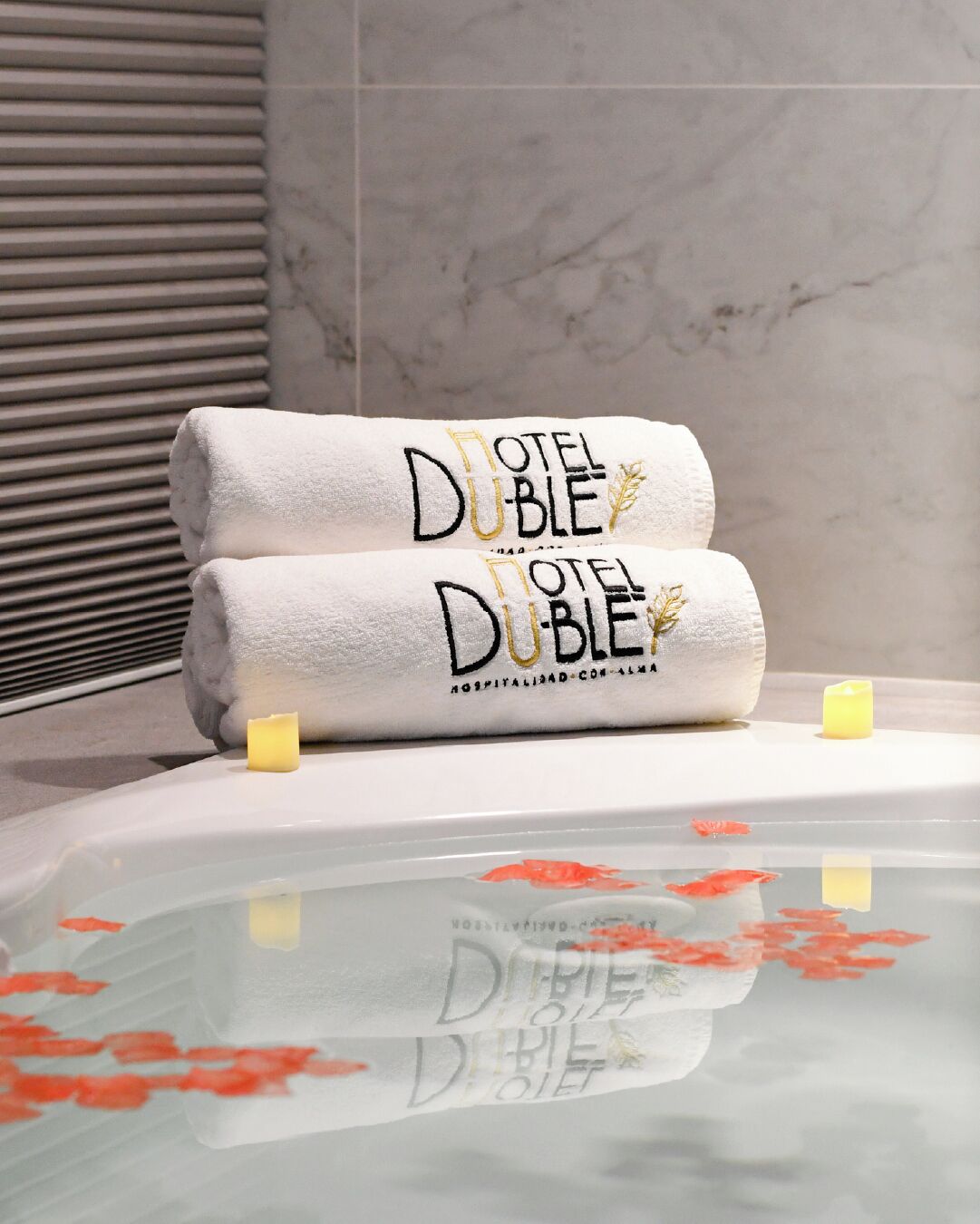A bathroom with a bathtub, two towels with 'HOTEL DUBLE' text, and a candle.
