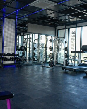 Un gimnasio con diversos equipos de ejercicio, incluyendo mancuernas, máquinas de pesas y una cinta de correr.