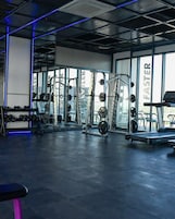 Un gimnasio con diversos equipos de ejercicio, incluyendo mancuernas, máquinas de pesas y una cinta de correr.
