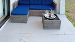 Une terrasse couverte avec un canapé d’angle bleu et une table sur laquelle se trouvent des verres et une bouteille.