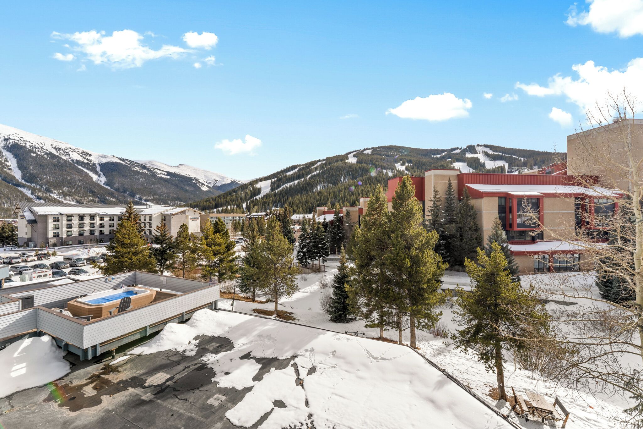 A hotel with a rooftop pool, surrounded by snow-covered mountains and trees.