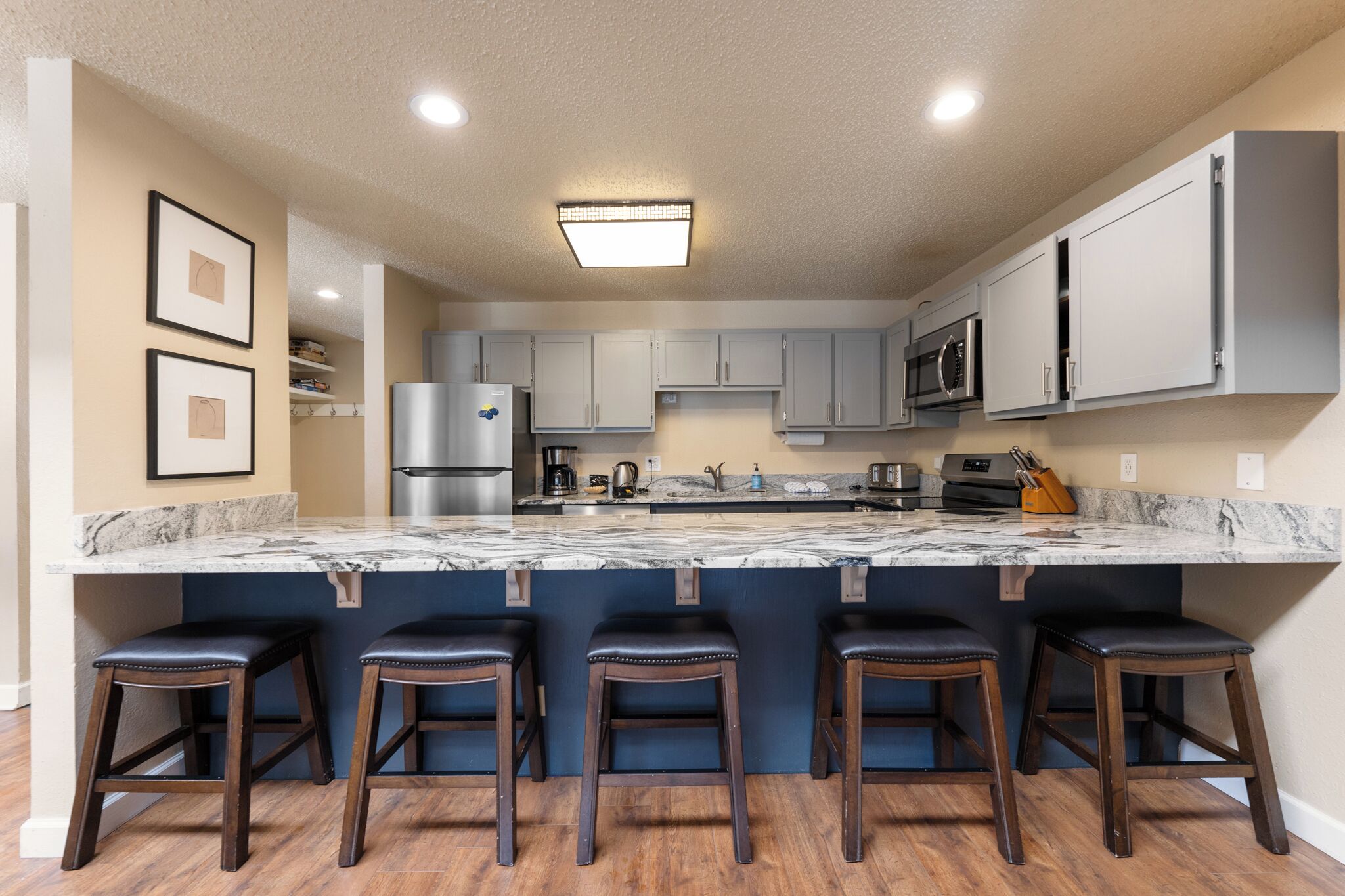 A modern kitchen with a marble countertop, stainless steel appliances, and bar stools.