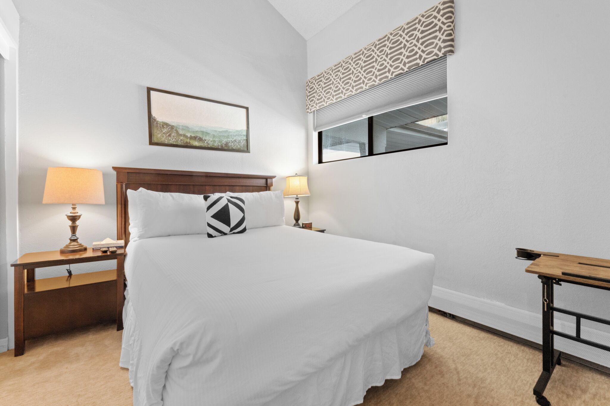 A neatly arranged hotel room with a large bed, bedside lamps, a small table, and a window with a view.