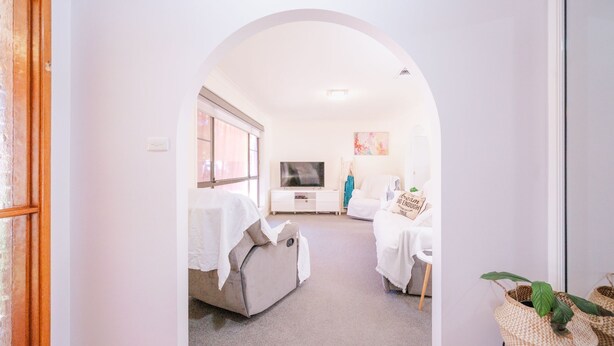 A bright, white room with a large window, a flat-screen TV, a sofa, and a small table. - Relaxing Family Escape 3-Bedroom Home in Oxley Vale (Oxley Vale)