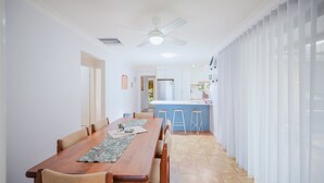 A dining area with a wooden table and chairs, a ceiling fan, and a kitchen in the background. - Relaxing Family Escape 3-Bedroom Home in Oxley Vale (Oxley Vale)
