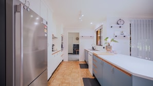 A modern kitchen with stainless steel appliances, wooden flooring, and a view into the dining area. - Relaxing Family Escape 3-Bedroom Home in Oxley Vale (Oxley Vale)