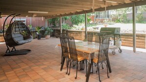 A covered patio with a wooden table and chairs, a hanging chair, and a grill. - Relaxing Family Escape 3-Bedroom Home in Oxley Vale (Oxley Vale)