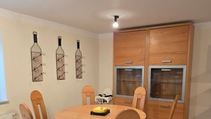 A dining area with a round wooden table and six chairs, a wooden cabinet with glass doors, and wall-mounted wine rack decorations. - Vacation apartment garden view (Schwarzach am Main)