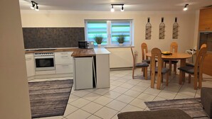 A modern kitchen with a central island, dining area with wooden chairs, and a small refrigerator. - Vacation apartment garden view (Schwarzach am Main)