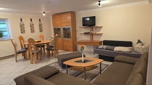 A modern living room with a sofa, dining table, chairs, a TV, and a wooden cabinet. - Vacation apartment garden view (Schwarzach am Main)