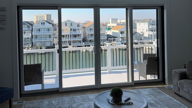 Ein geräumiges Wohnzimmer mit einer großen Schiebeglastür, die auf einen Balkon führt, einem Deckenventilator und einem runden Couchtisch mit einer Pflanze.