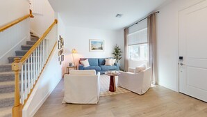 A living room with a staircase, a blue sofa, two white armchairs, a small table, and a plant. - Cozy & Spacious 5BR 4.5B Furnished Home w/ Loft & Large Backyard (North Fort Myers)