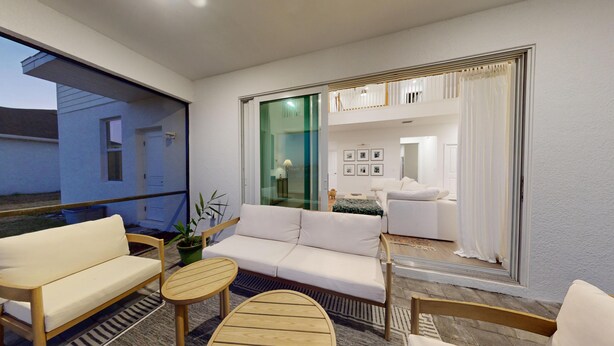 A modern living room with a white sofa, a wooden coffee table, and a glass door leading to a balcony. - Cozy & Spacious 5BR 4.5B Furnished Home w/ Loft & Large Backyard (North Fort Myers)