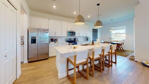 A modern kitchen with white cabinets, stainless steel appliances, and a central island with bar stools. - Cozy & Spacious 5BR 4.5B Furnished Home w/ Loft & Large Backyard (North Fort Myers)