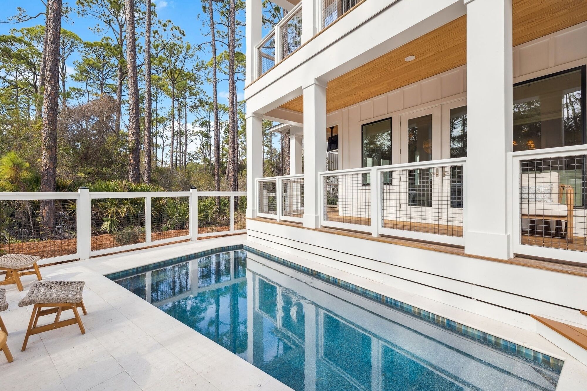 Una casa moderna con piscina, barandillas blancas y vista a árboles altos.