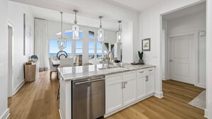 A modern kitchen with a large island, stainless steel dishwasher, white cabinetry, and pendant lighting. - Top-Floor Gulf Views and Beach Access (Seacrest)