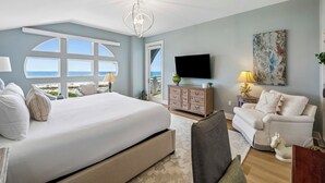 A bedroom with a large bed, a TV, a sofa, and a view of the sea. - Top-Floor Gulf Views and Beach Access (Seacrest)