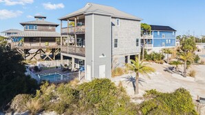 Ein Strandgrundstück mit einem zweistöckigen Gebäude, einer Holzterrasse mit Pool und einem blauen Haus im Hintergrund.