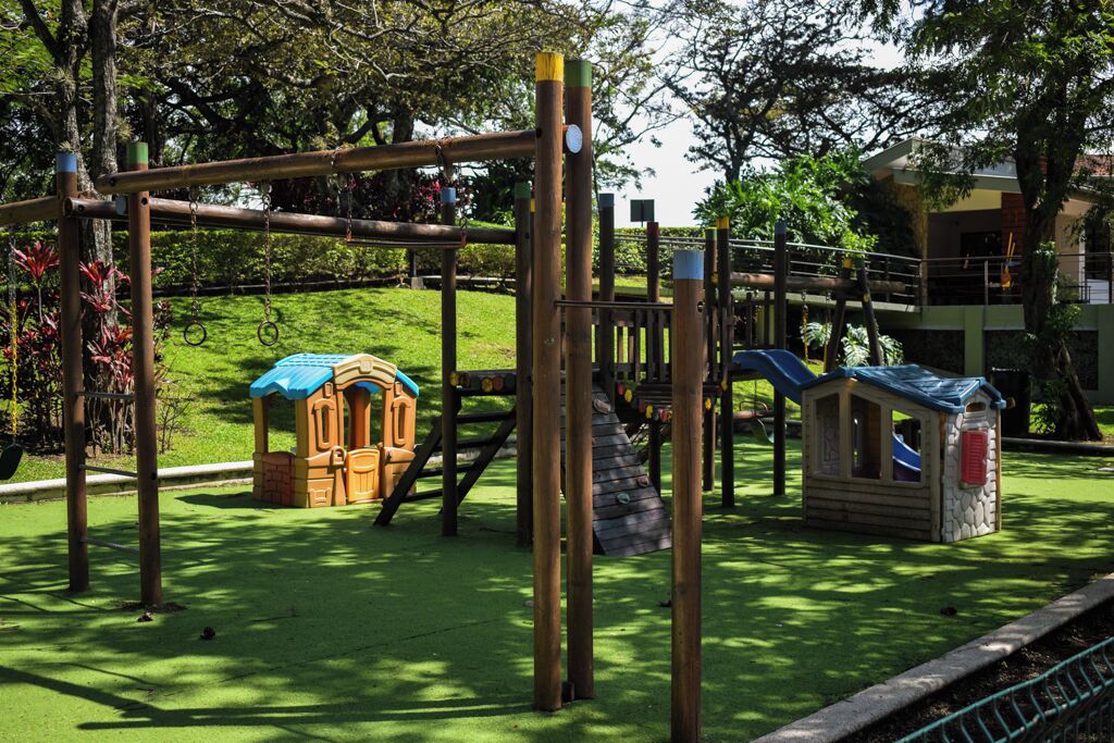 Ein Spielplatz mit einer Holzschaukel, einer Rutsche und einem kleinen Spielhäuschen.