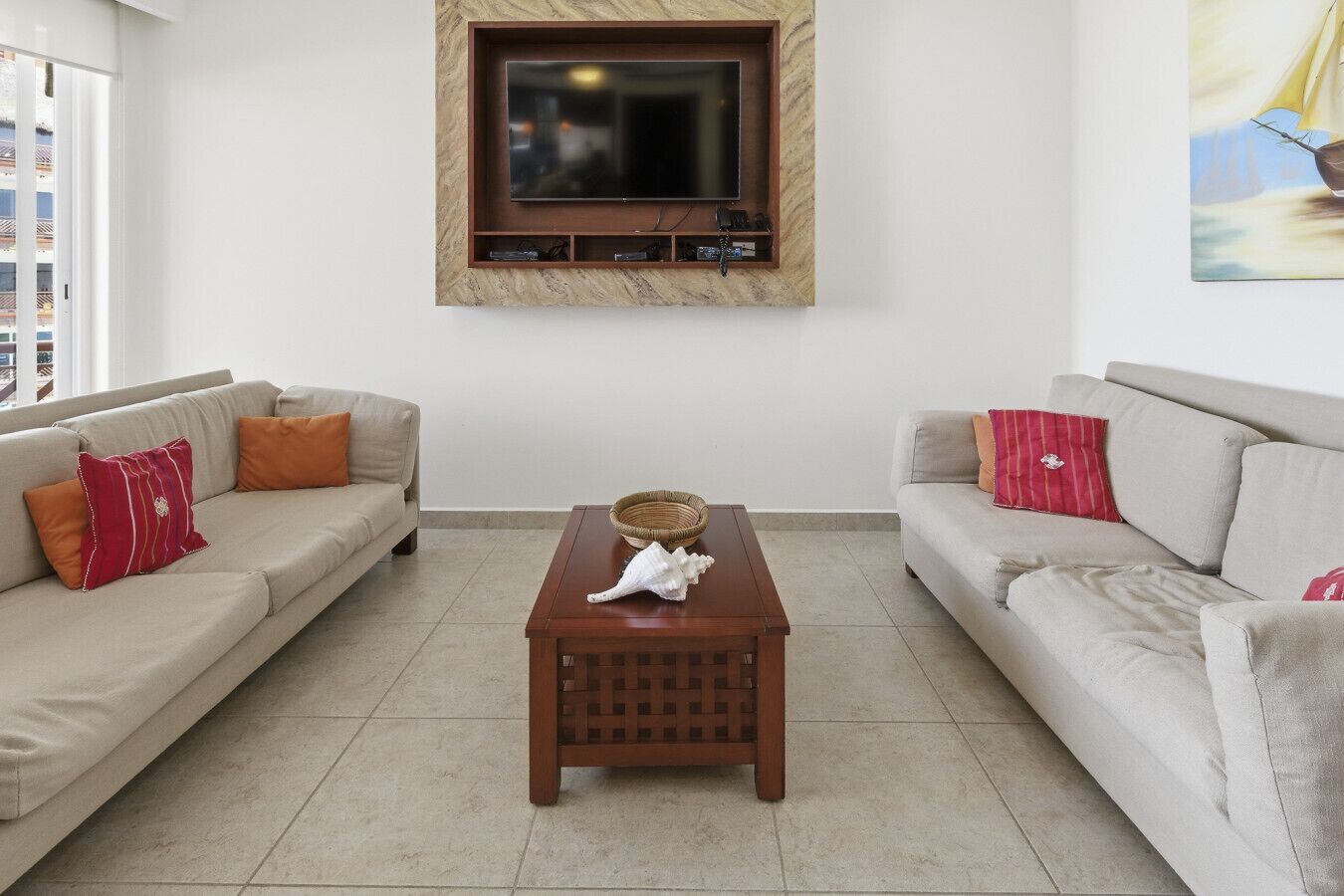 Ein Wohnzimmer mit zwei Sofas, einem Couchtisch, einem an der Wand montierten Fernseher und einem Wandbild.