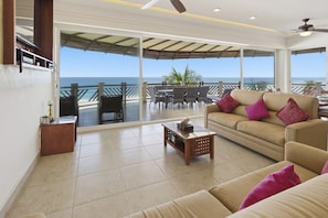 A spacious living area with a large window overlooking the sea, a sofa with cushions, a coffee table, and a dining area with chairs and a table.
