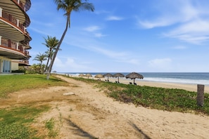 A beach with a hotel, palm trees, and thatched umbrellas.