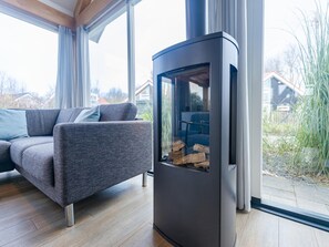 Ein modernes Wohnzimmer mit einer Couch, einem Kamin mit Holz und Blick ins Freie durch große Fenster.