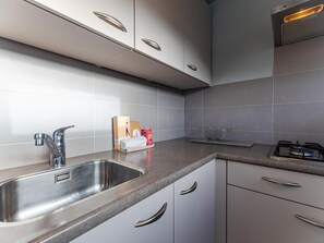 A modern kitchen with a stainless steel sink, a gas stove, and white cabinetry. - Comfortable Family Home on the Beach (Renesse)