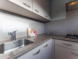 Una cocina moderna con un lavamanos de acero inoxidable, una estufa a gas y armarios blancos.
