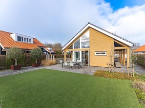 A modern house with a sloped roof, a patio with outdoor furniture, and a well-maintained lawn. - Comfortable Family Home on the Beach (Renesse)
