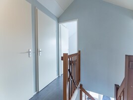 Un pasillo con barandilla de madera, una puerta y vista a una habitación contigua.